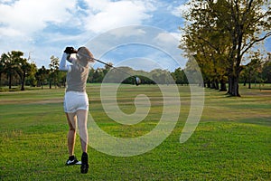 Healthy Sport. Asian Sporty woman golfer player doing golf swing tee off on the green evening time, she presumably does exercise.