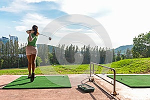 Healthy Sport.  Asian sporty woman swing golf ball practice at golf driving range on evening on time for healthy sport. photo