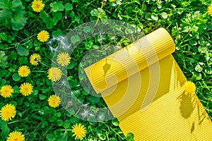 Yellow yoga mat on grass with dandelions