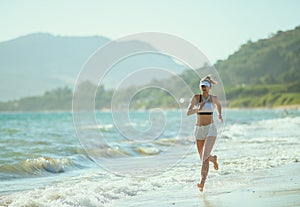 Healthy sports woman on ocean shore in evening jogging