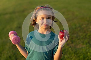 Healthy sporty child with apple and dumbbell outdoor in park. Child workout. Kid sport. Child exercising with dumbbells