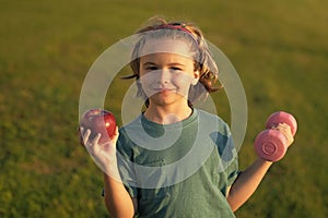 Healthy sporty child with apple and dumbbell outdoor in park. Child workout. Kid sport. Child exercising with dumbbells