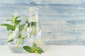 Healthy spring beverage in bottle and glass with green cucumber, mint, lime, straw on soft blue wooden background.