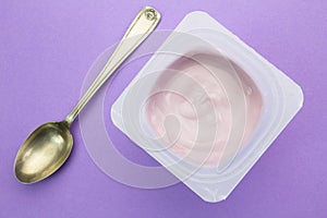 Healthy strawberry fruit flavored yoghurt with natural coloring in plastic cup isolated on purple background