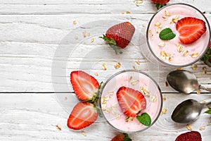 Healthy strawberry yogurt with oats and mint in glasses with fresh berries and spoons over white wooden table