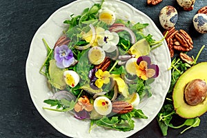 Healthy summer salad with quail eggs, avocado, pecans, wild rocket, red onion and edible viola flowers.