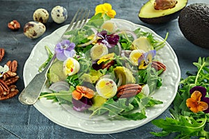 Healthy summer salad with quail eggs, avocado, pecans, wild rocket, red onion and edible viola flowers.