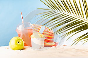 Healthy summer vacation and relaxation on tropical beach with cold drink, ice cream, fruit and sun hat under palm leaves with sun.