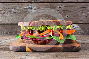 Healthy superfood sandwich with avocado, beet hummus, spinach radishes and carrots on a wooden board against rustic wood