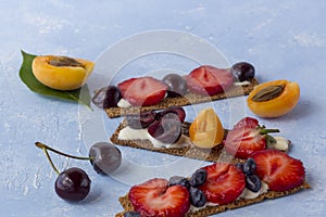 Healthy and tasty toasts with curd cheese, fruits and berries on a blue background