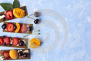 Healthy and tasty toasts with curd cheese, fruits and berries on a blue background