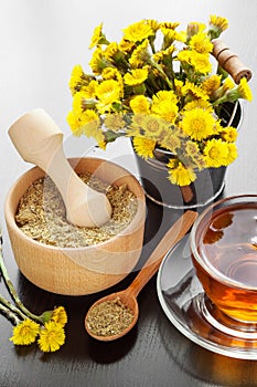 Healthy tea, bucket with coltsfoot flowers and wooden mortar on