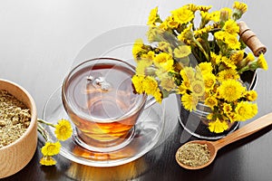 Healthy tea in glass cup closeup, bucket with coltsfoot flowers