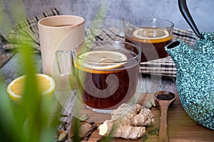 Healthy tea poured into transparent cup. Teapot, lemon, ginger, cardamom, heather bunch and glass jar