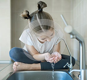 Healthy thirsty caucasian child drinking from water tap or faucet in kitchen. Hands open for drinking tap water. Pouring clean