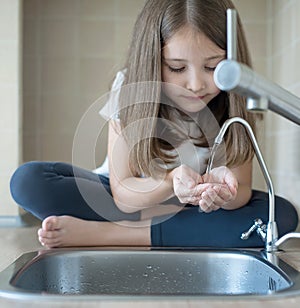 Healthy thirsty child is drinking from water tap or faucet in kitchen. Drinking tap water is preserving your health, more