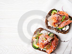 Healthy toasts with rye bread with cream cheese, salmon, fresh cucumber, capers, sesame seeds, black pepper and arugula on white