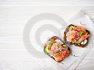 Healthy toasts with rye bread with cream cheese, salmon, fresh cucumber, capers, sesame seeds, black pepper and arugula on white