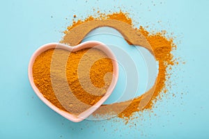 Healthy turmeric powder in a white heart shaped bowl on blue background