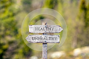 Healthy unhealthy text carved on wooden signpost outdoors in nature.