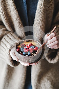 Healthy vegan breakfast bowl with oats, berries in womans hands