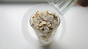 Healthy vegan breakfast, oatmeal porridge. Hand of a Caucasian man pours large oatmeal from one glass into another on a