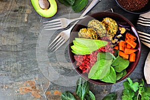 Healthy vegan buddha bowl with falafels, beet quinoa, avocado, and vegetables on dark stone, corner border with copy space.
