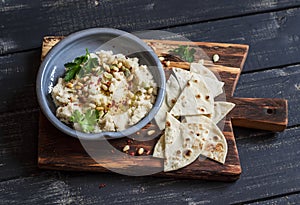 Healthy vegan cauliflower hummus and homemade tortilla on a dark rustic cutting board on a dark background.