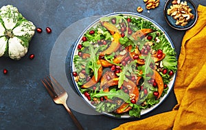 Healthy vegan eating, autumn pumpkin salad with baked honey pumpkin slices, lettuce, arugula, pomegranate seeds and walnuts.