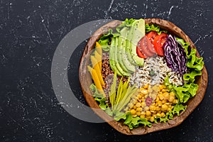 Healthy vegan food bowl with quinoa, wild rice, chickpea, tomatoes, avocado, greens, cabbage, lettuce on black stone background
