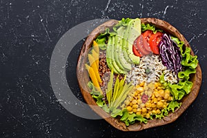 Healthy vegan food bowl with quinoa, wild rice, chickpea, tomatoes, avocado, greens, cabbage, lettuce on black stone background photo