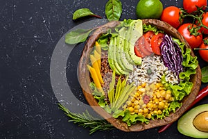 Healthy vegan food bowl with quinoa, wild rice, chickpea, tomatoes, avocado, greens, cabbage, lettuce on black stone background photo