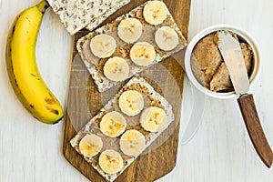 Healthy vegan homemade chunky peanut butter and banana sandwich with Swedish whole grain crispbread on wood cutting board,knife