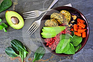 Healthy vegan lunch bowl with falafels, beet quinoa, avocado, and vegetables over dark stone