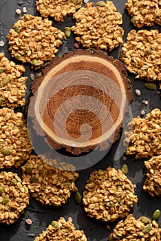 Healthy vegan snack concept. Oatmeal breakfast cookies and round wood slab on black background top view