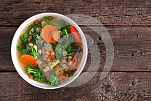 Healthy vegetable soup with kale and lentils, overhead view on wood