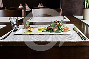 Healthy vegetable summer salad, fresh vegetables and dressing with grilled cheese flambe arranged on plate dinner table