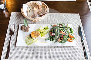 Healthy vegetable summer salad, fresh vegetables and dressing with grilled cheese flambe arranged on plate dinner table