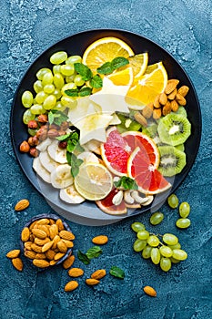 Healthy vegetarian bowl dish with fresh fruits and nuts. Plate with raw apple, orange, grapefruit, banana, kiwi, lemon, grape, alm