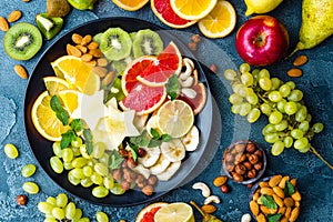 Healthy vegetarian bowl dish with fresh fruits and nuts. Plate with raw apple, orange, grapefruit, banana, kiwi, lemon, grape, alm