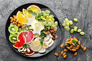 Healthy vegetarian bowl dish with fresh fruits and nuts. Plate with raw apple, orange, grapefruit, banana, kiwi, lemon, grape, alm