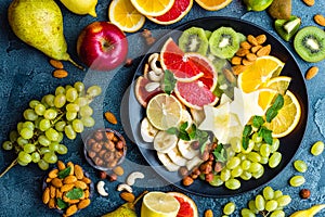 Healthy vegetarian bowl dish with fresh fruits and nuts. Plate with raw apple, orange, grapefruit, banana, kiwi, lemon, grape, alm