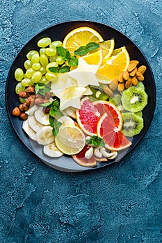 Healthy vegetarian bowl dish with fresh fruits and nuts. Plate with raw apple, orange, grapefruit, banana, kiwi, lemon, grape, alm