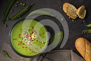 Healthy vegetarian creamy green peas soup with toasted garlic bread, spoon on the table in rustic style. Fresh pea pods