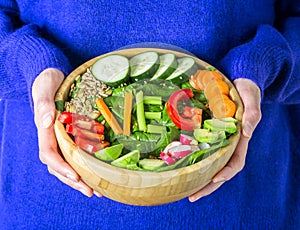 Healthy vegetarian dinner. Woman in warm sweater holding bowl with fresh salad, avocado, cereals, beans, vegetables and word