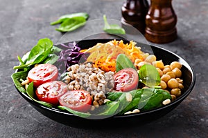 Healthy vegetarian dish with buckwheat and vegetable salad of chickpea, kale, carrot, fresh tomatoes, spinach leaves and pine nuts