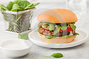 Healthy vegetarian meat free burger on round ceramic plate with vegetables and spinach on light table background