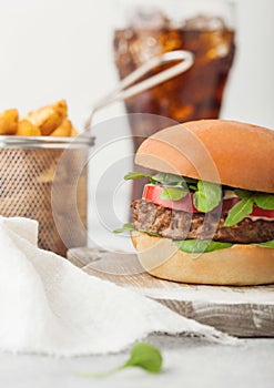 Healthy vegetarian meat free burger on round chopping board with vegetables on light table background with potato wedges and glass