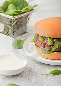 Healthy vegetarian meat free burger on round chopping board with vegetables and spinach on light table background with organic