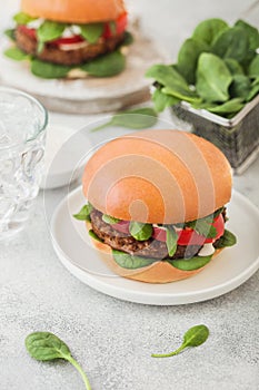 Healthy vegetarian meat free burgers on round ceramic plate with vegetables and spinach on light table background with glass of photo